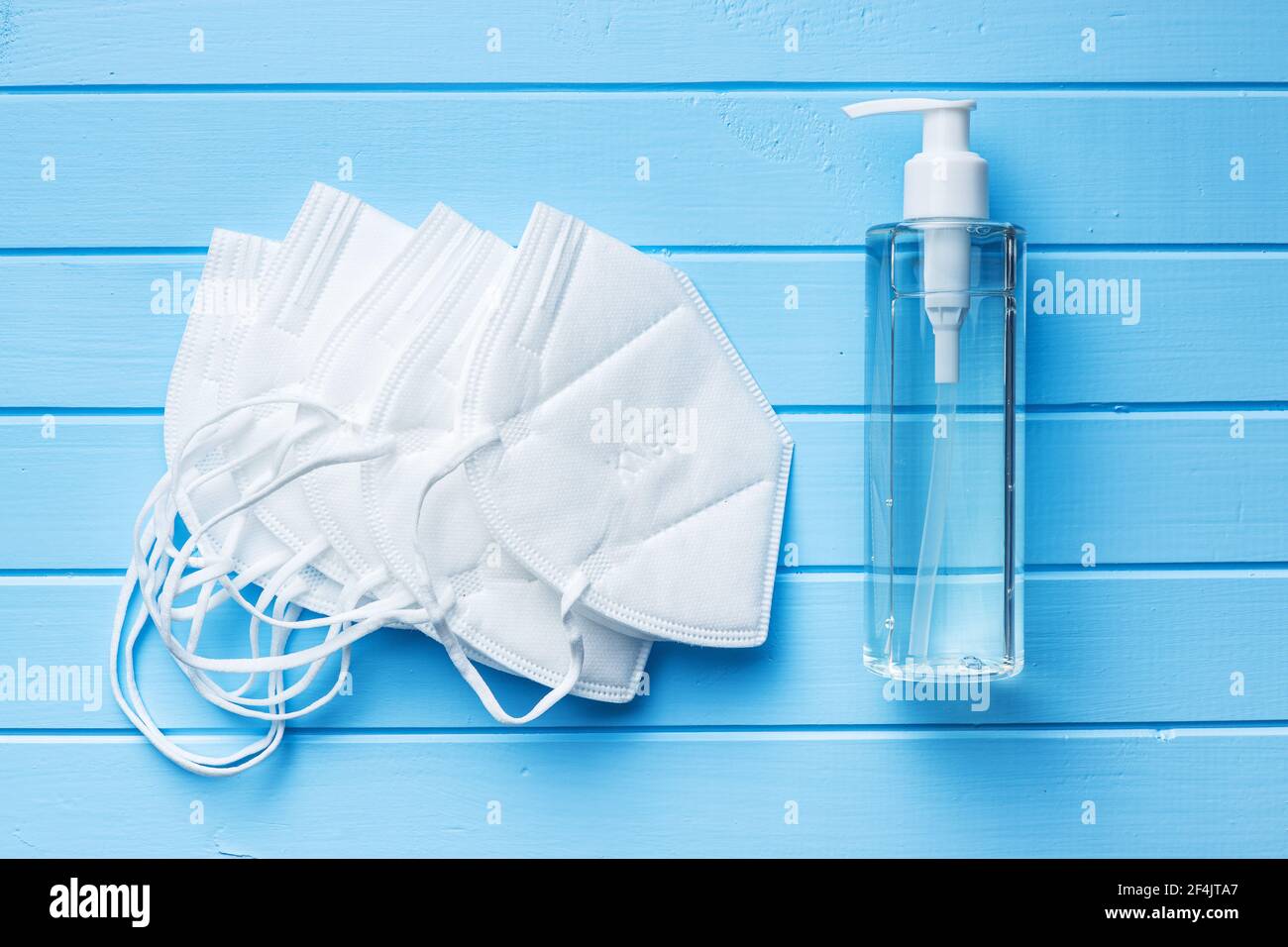 Coronavirus prevention hand sanitizer and kn95 respirator mask. Hand disinfectant gel in pump bottle on blue table. Top view. Stock Photo