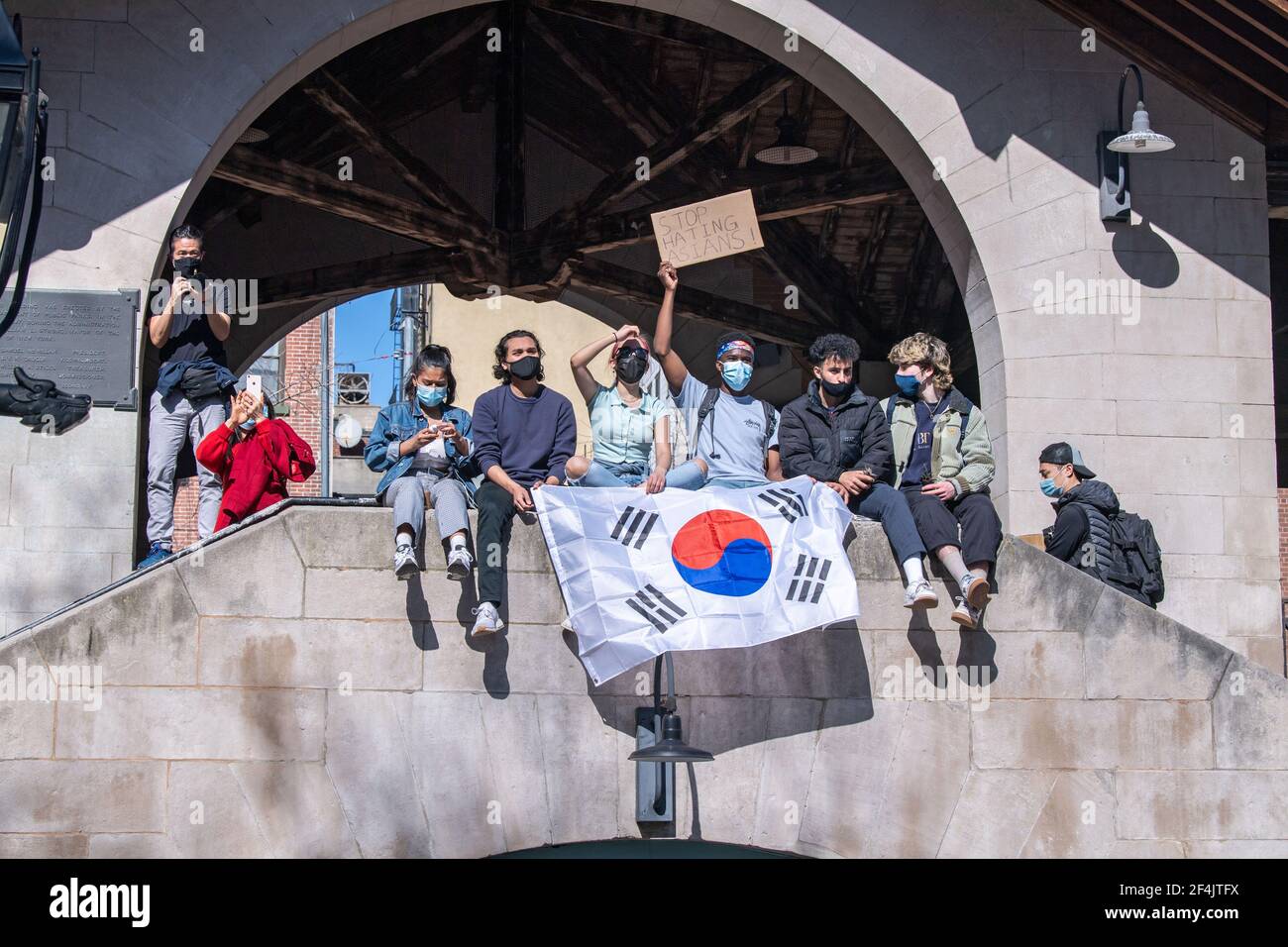 Protesters sit in on a structure over looking the park with a sign that says Stop Hating Asians and Korean flag during a rally against hate in Columbus Park in the Chinatown neighbourhood of Manhattan in New York City.A rally for solidarity was organized in response to a rise in hate crimes against the Asian community since the start of the coronavirus (COVID-19) pandemic in 2020. On March 16 in Atlanta, Georgia, a man went on a shooting spree in three spas that left eight people dead, including six Asian women. Stock Photo