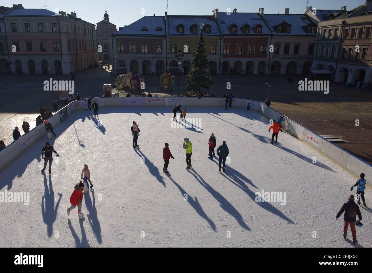 Zamosc, Poland, December 27, 2020. Townspeople skate on an ice skating rink on a sunny winter morning. Skating rink in the central square of the city. Stock Photo