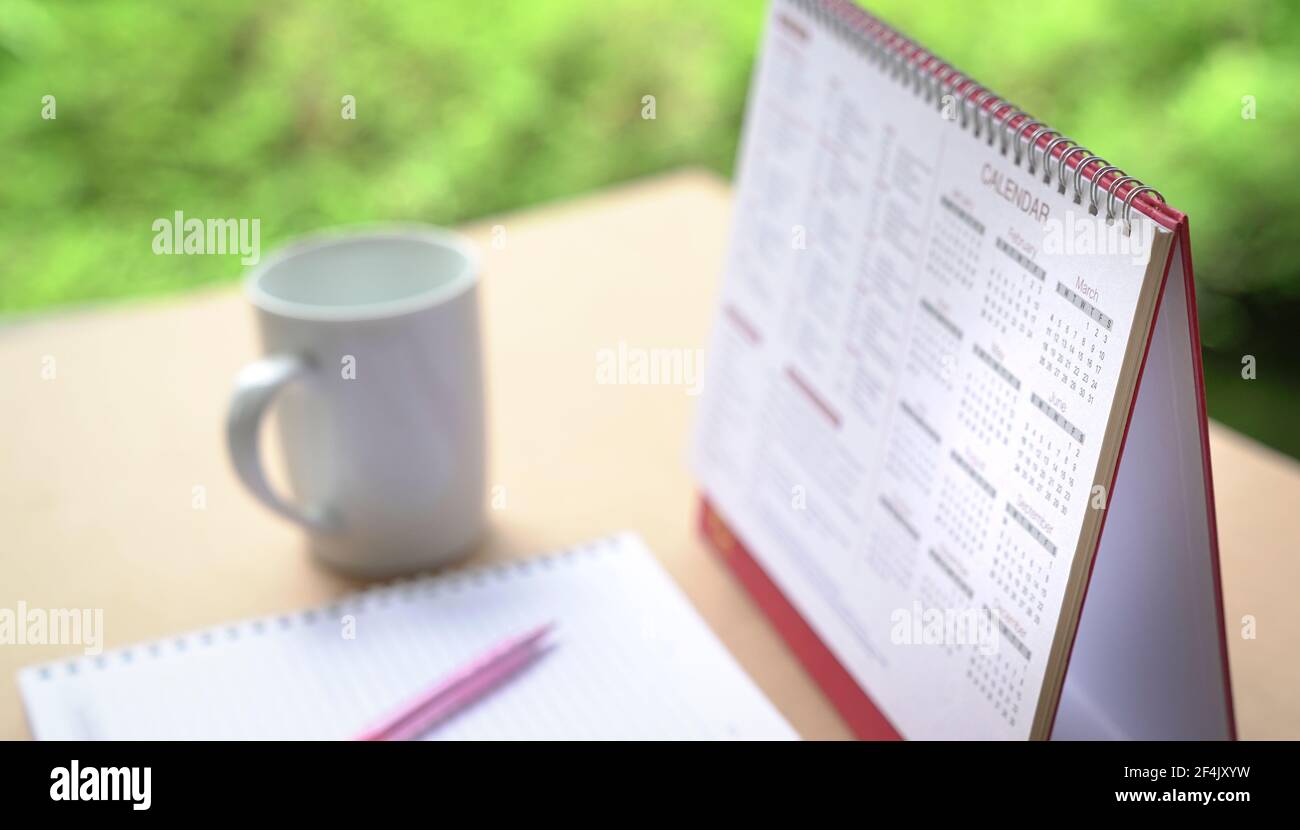 Calendar on table with cup of coffee and notebbok, Selective focus. Green nature at the background. Stock Photo