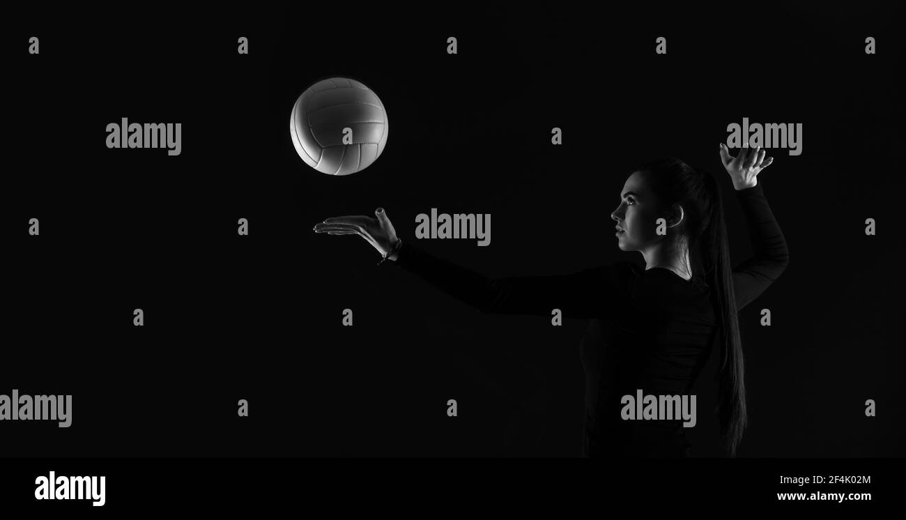 Volleyball girl kick ball on dark background. Player doing sport workout online. Sport and recreation concept. Black and white color filter Stock Photo