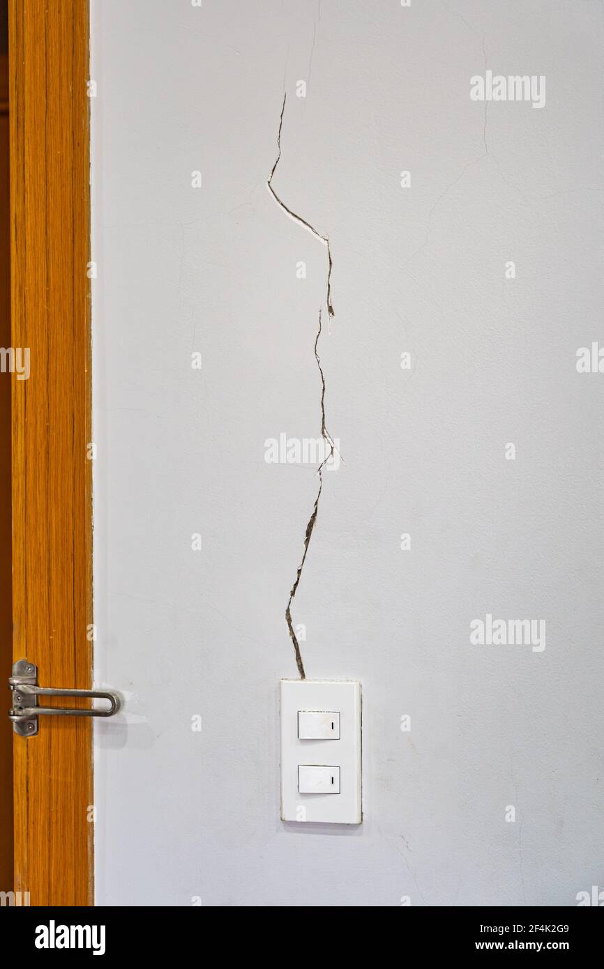 Cracked white cement wall near light switch and the door Stock Photo