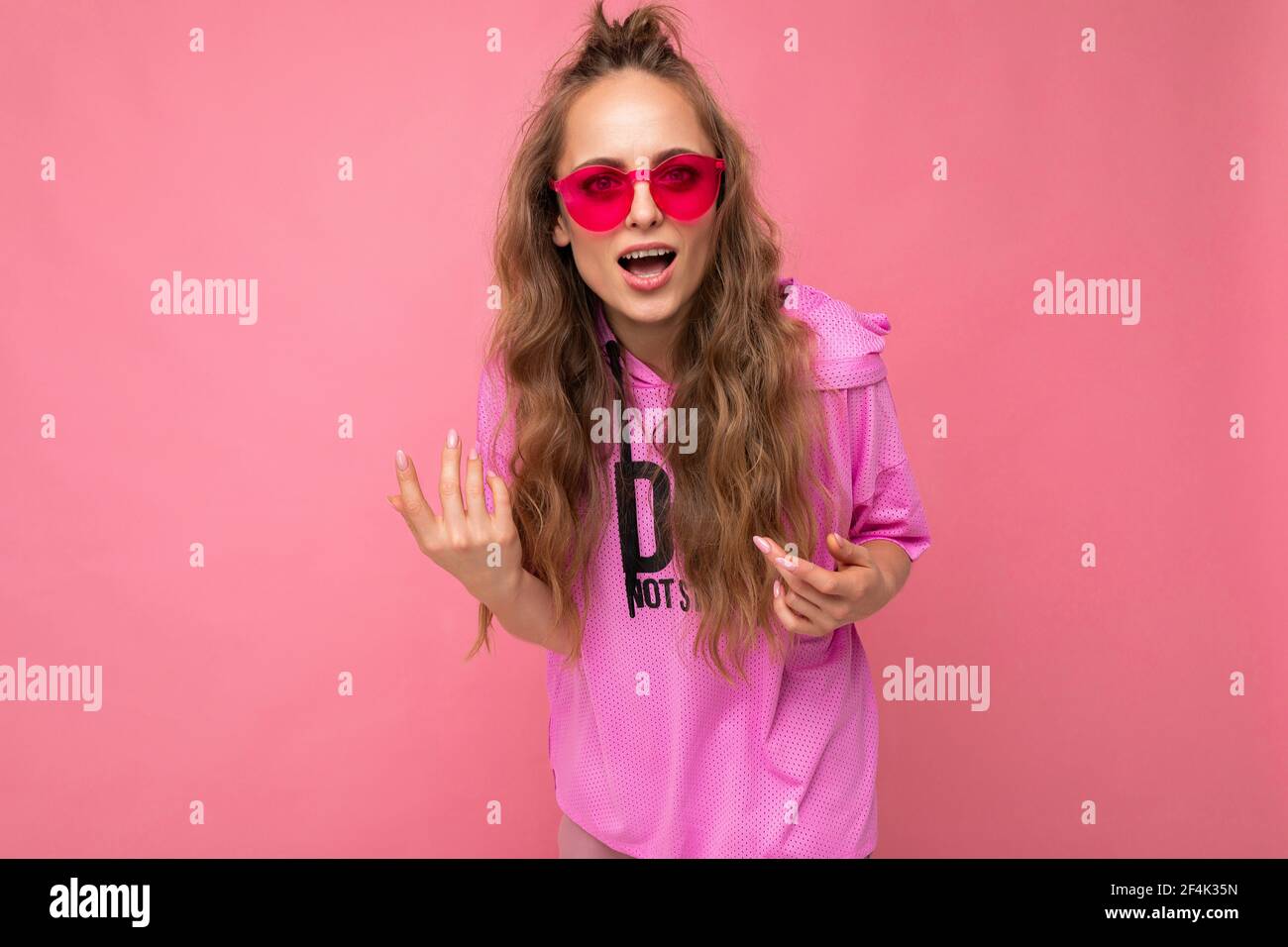 Photo shot of beautiful surprised young dark blonde woman wearing casual clothes and stylish sunglasses isolated over colorful background looking at Stock Photo