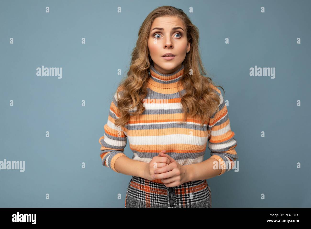 Photo portrait of young attractive beautiful sad upset touchy blonde woman with sincere emotions wearing striped pullover isolated on blue background Stock Photo
