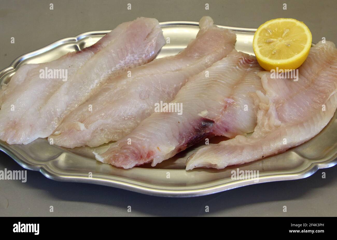 Raw fish filet and half lemon on a pewter dish Stock Photo