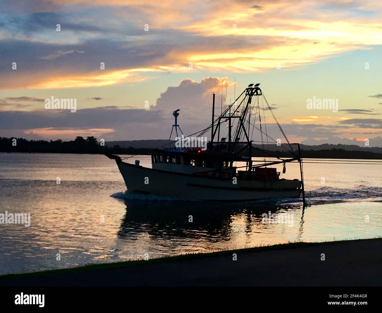 Trawler heads out under Autumn sunset on the Richmond River at Ballina Stock Photo