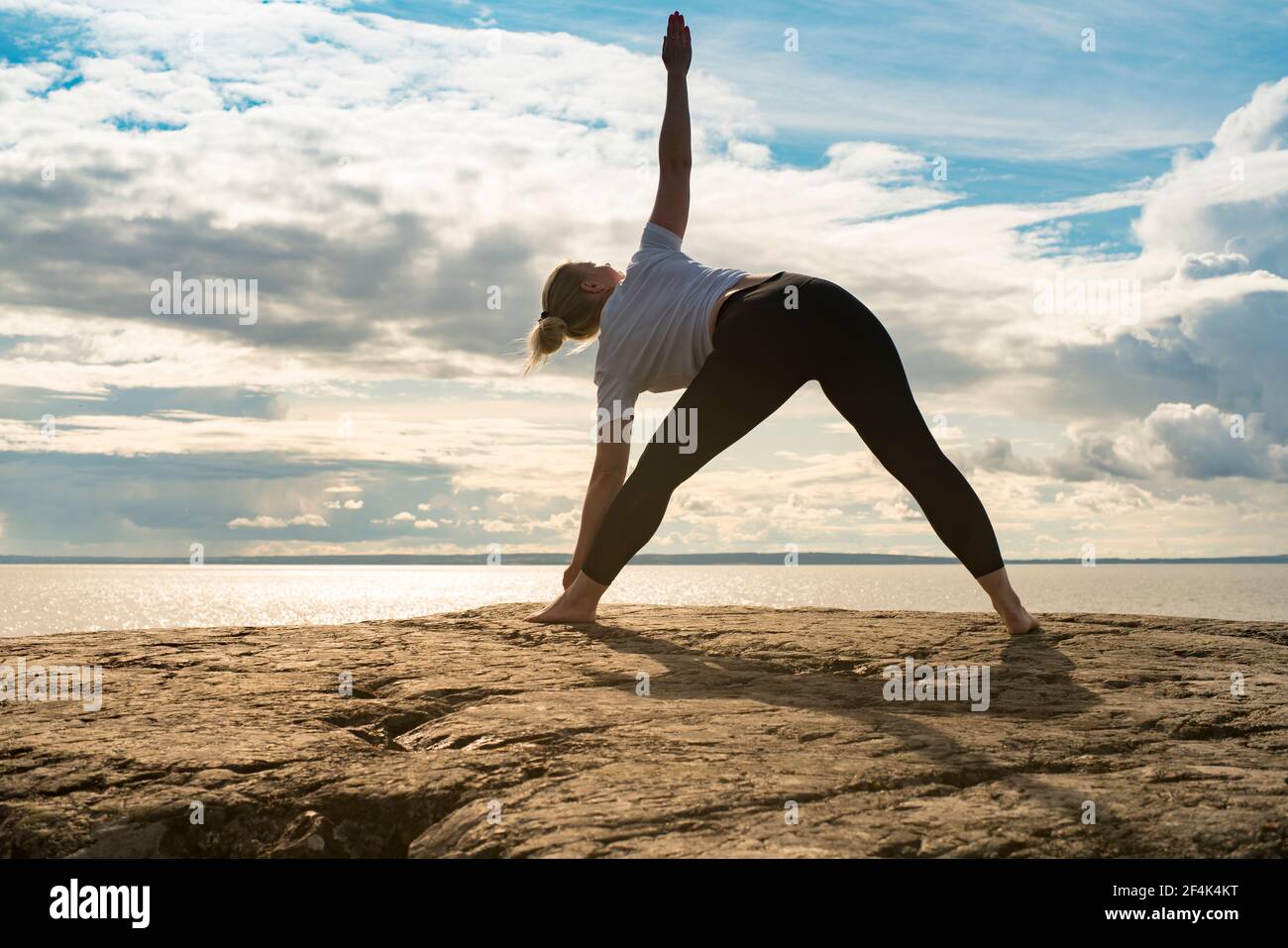 Woman practicing Yoga, meditation or stretching next to water on cliff Stock Photo