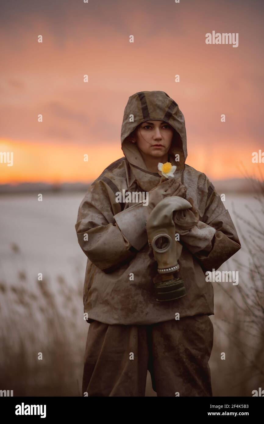 A young woman with a flower in her hands. The woman in the protective suit took off her gas mask.  Stock Photo