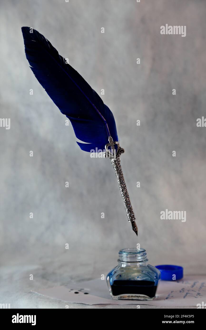 An ink bottle and a decorative and shiny quill with blue feather in the air Stock Photo