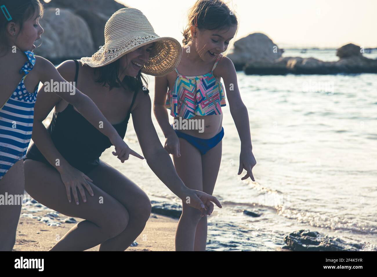 Mom and two little daughters are walking along the seashore in ...