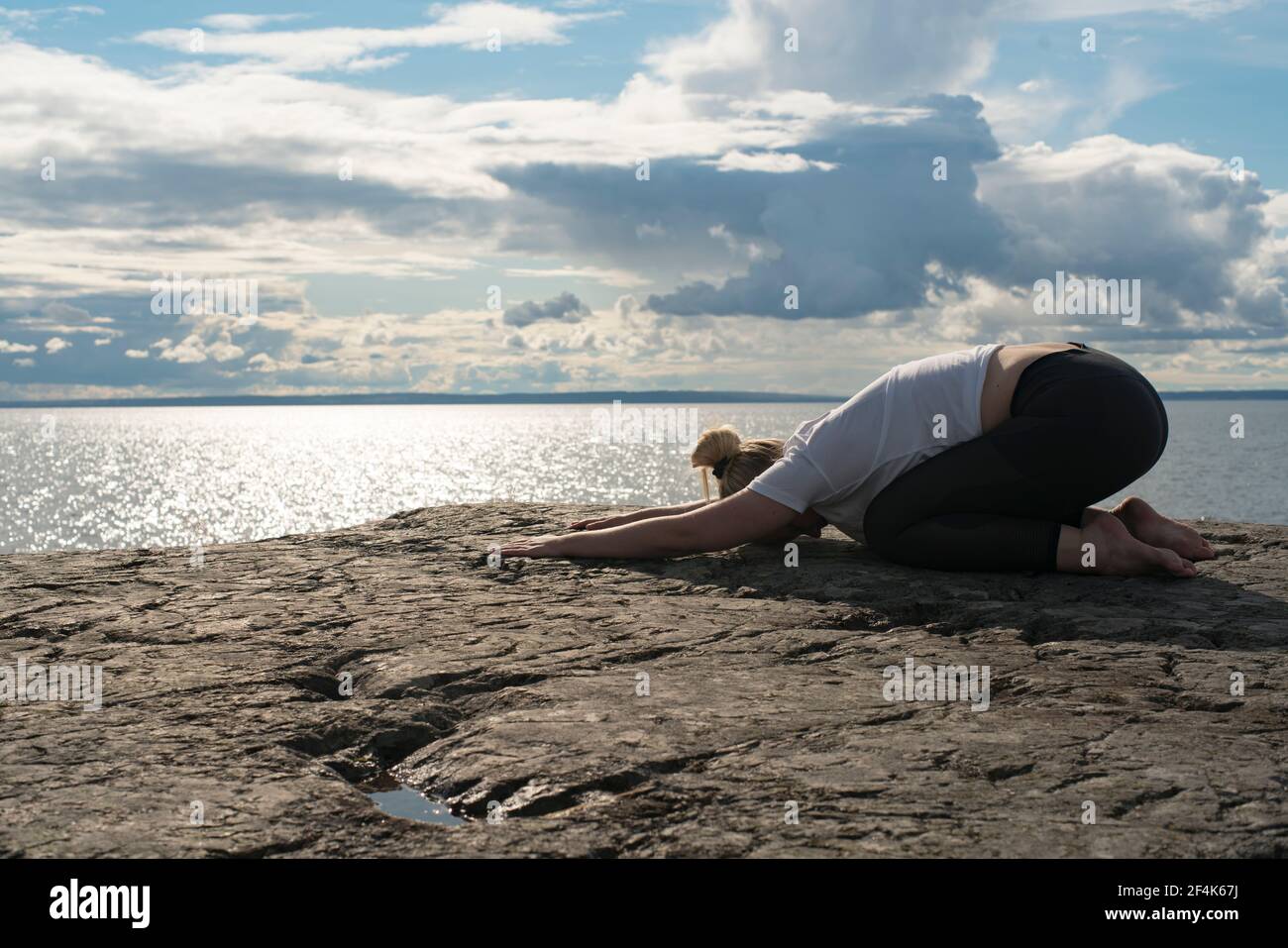 Woman practicing Yoga, meditation or stretching next to water on cliff Stock Photo