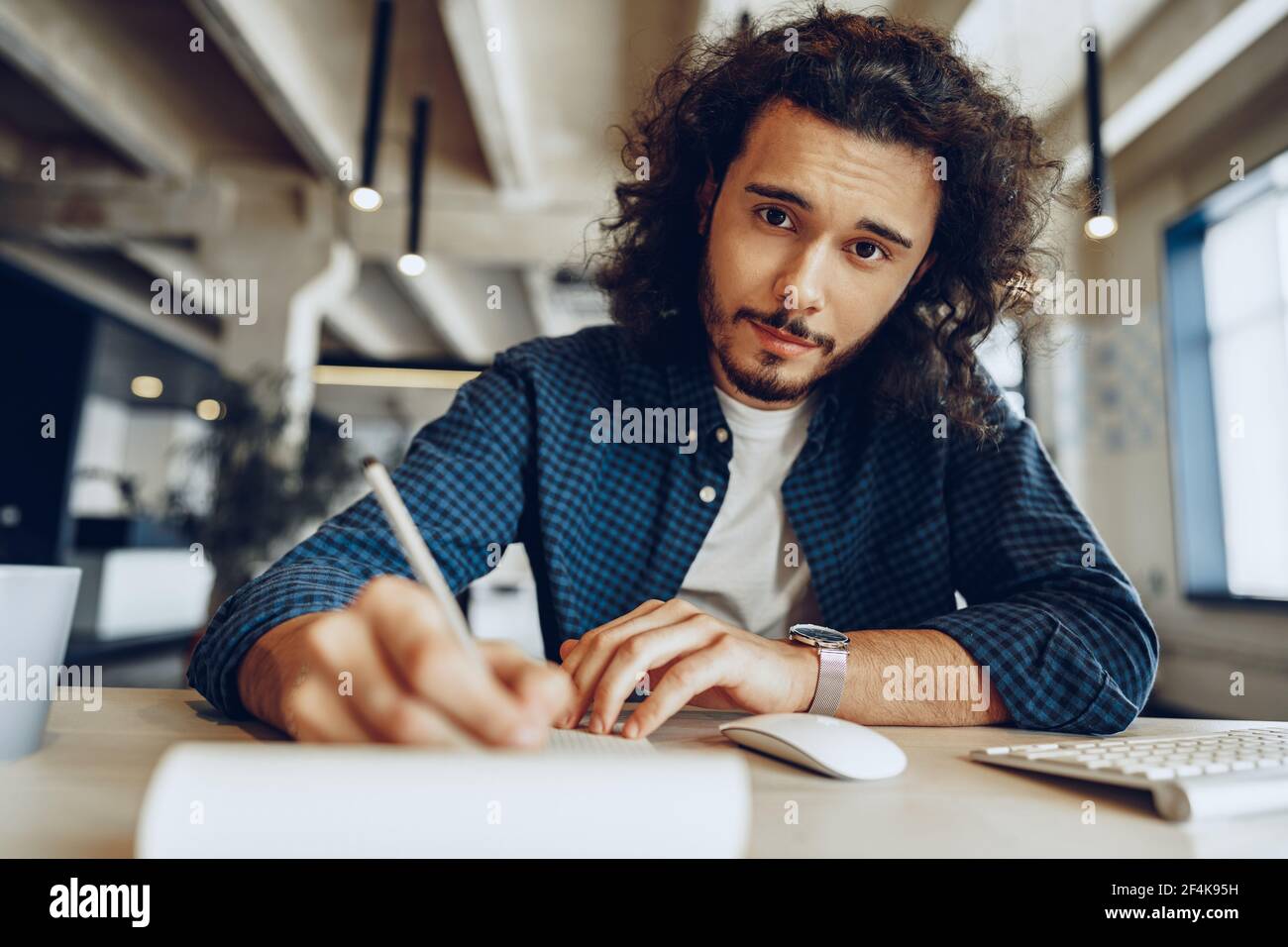 Handsome curly guy is making notes at the working table in open space office Stock Photo