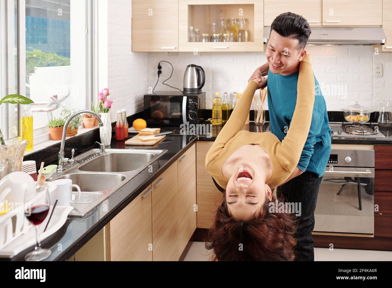 Happy young Vietnamese couple in love enjoying dancing in kitchen when cooking dinner together Stock Photo