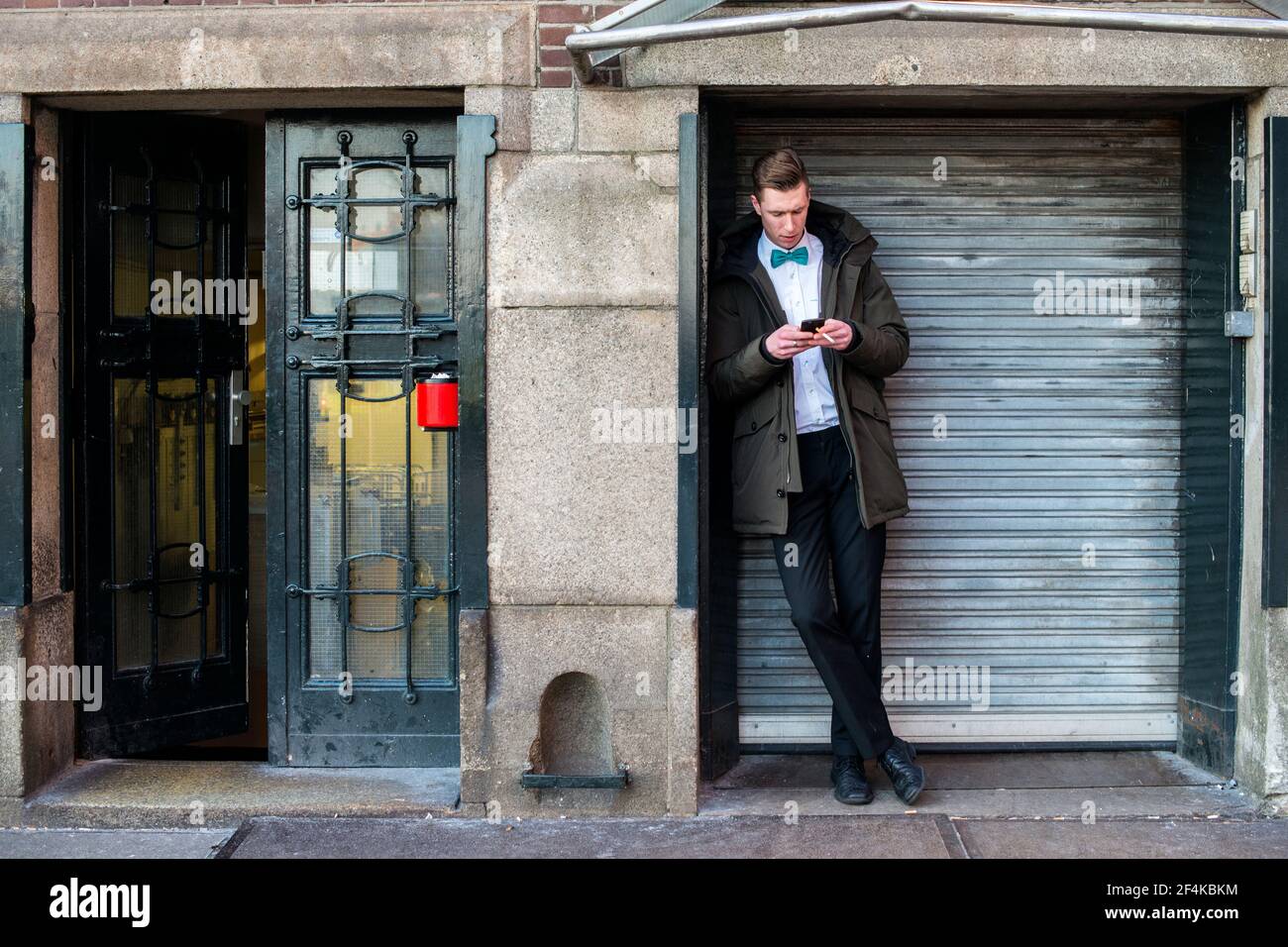 Rotterdam, Netherlands. Hotel employee using his break from work to smoke a  cigarette and to use his smartphone Stock Photo