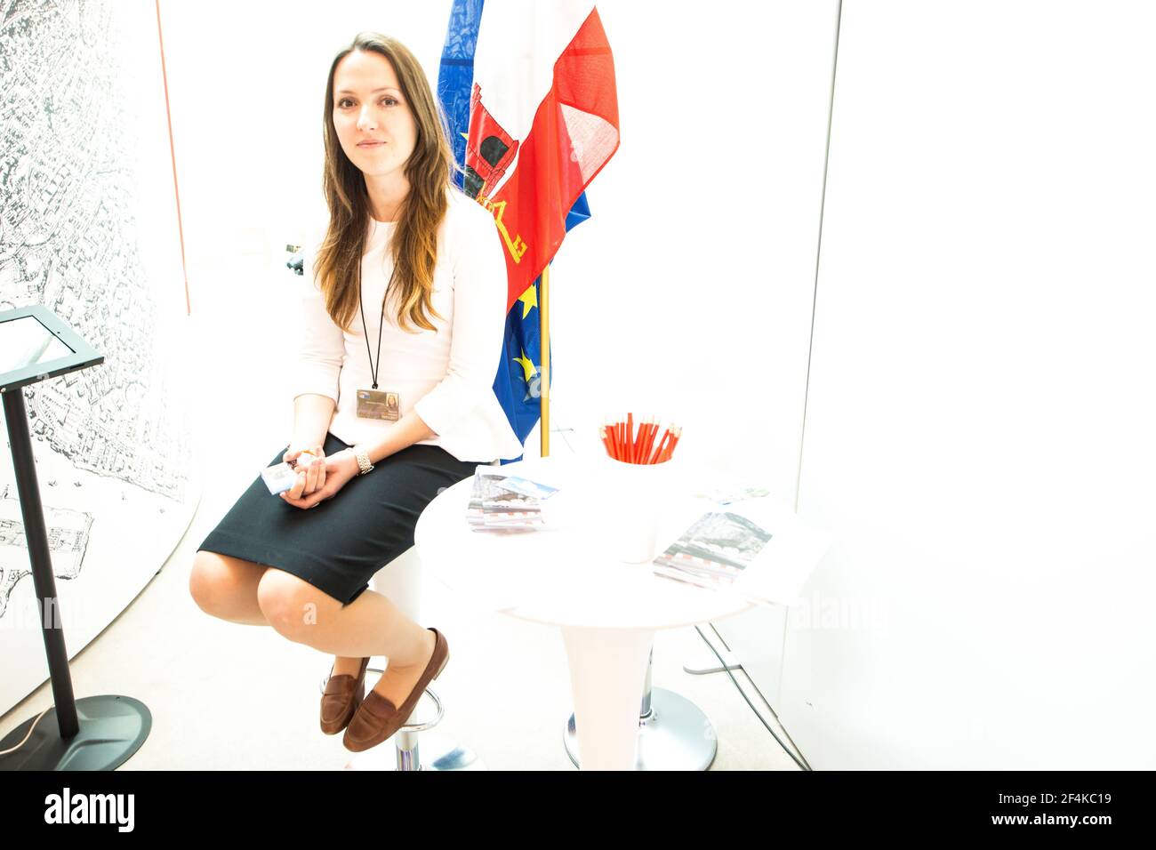 European Parliament, Brussels. Young, attractive brunette sitting in front of her Gibraltar country flags inside the Parliament building. Stock Photo