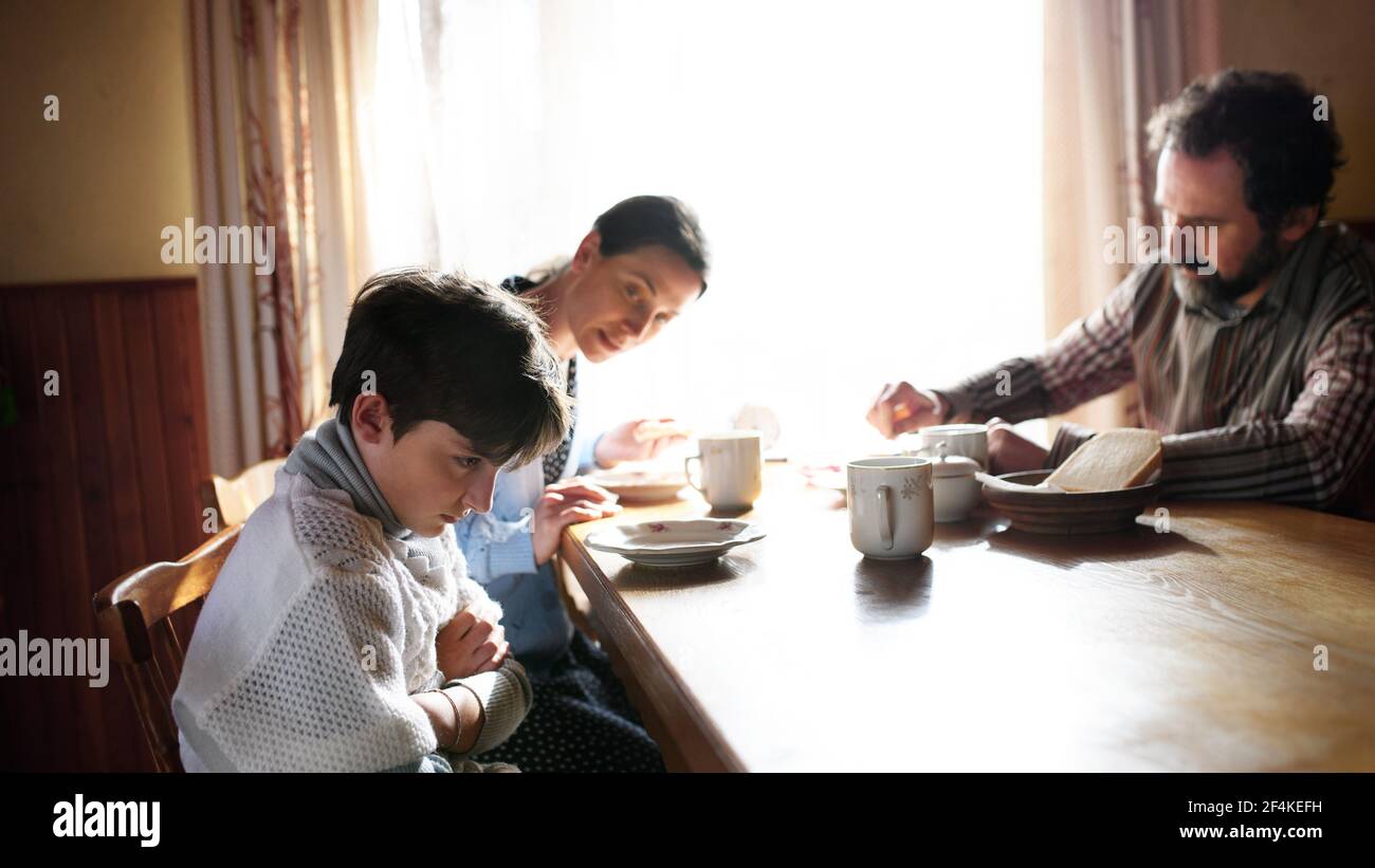 Angry small girl with parents sulking indoors at the table at home, poverty concept. Stock Photo