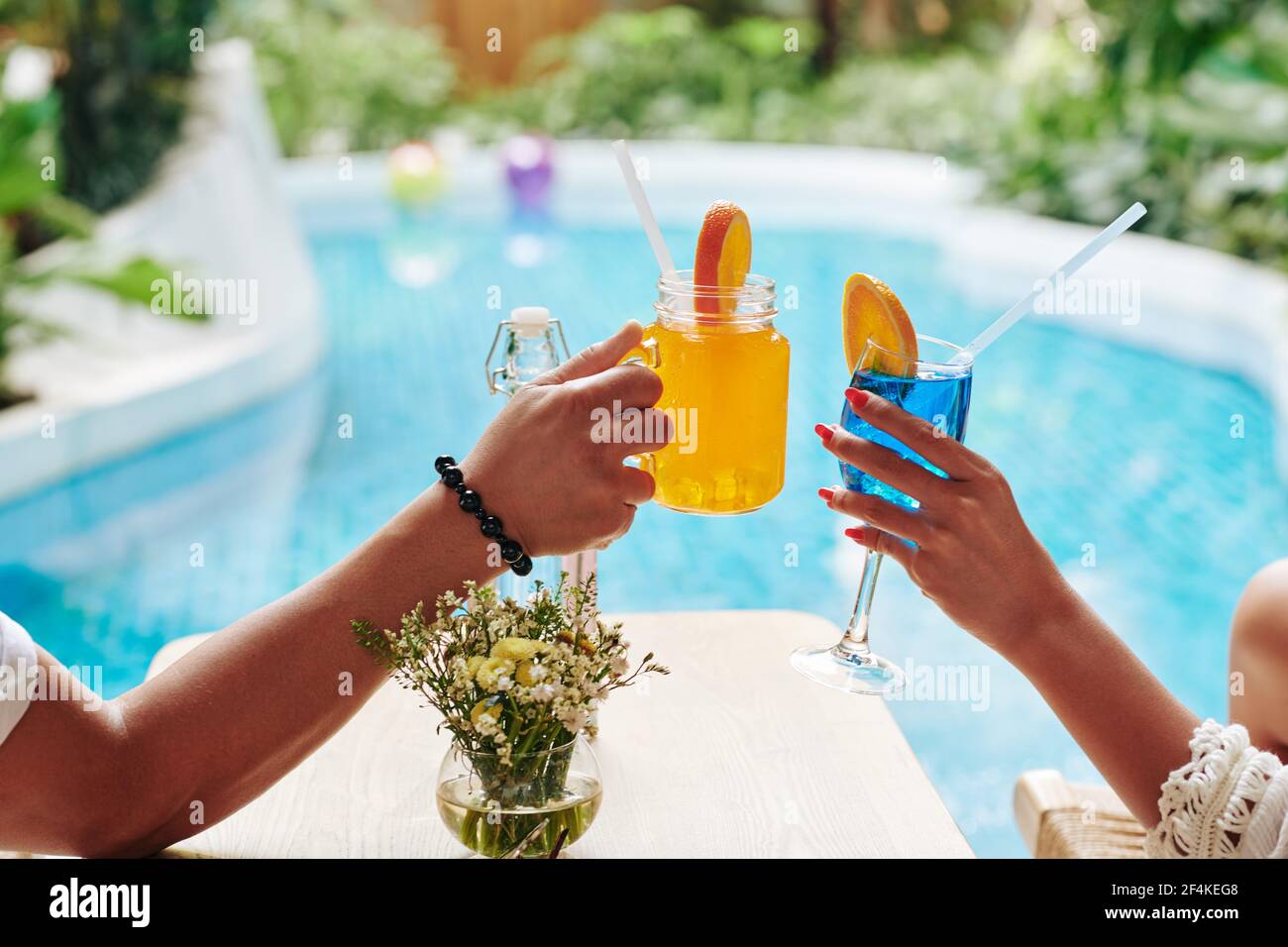 Hands of man and woman clinking glasses of sweet fruit cocktails when  enjoying sunbathing by swimming pool Stock Photo - Alamy