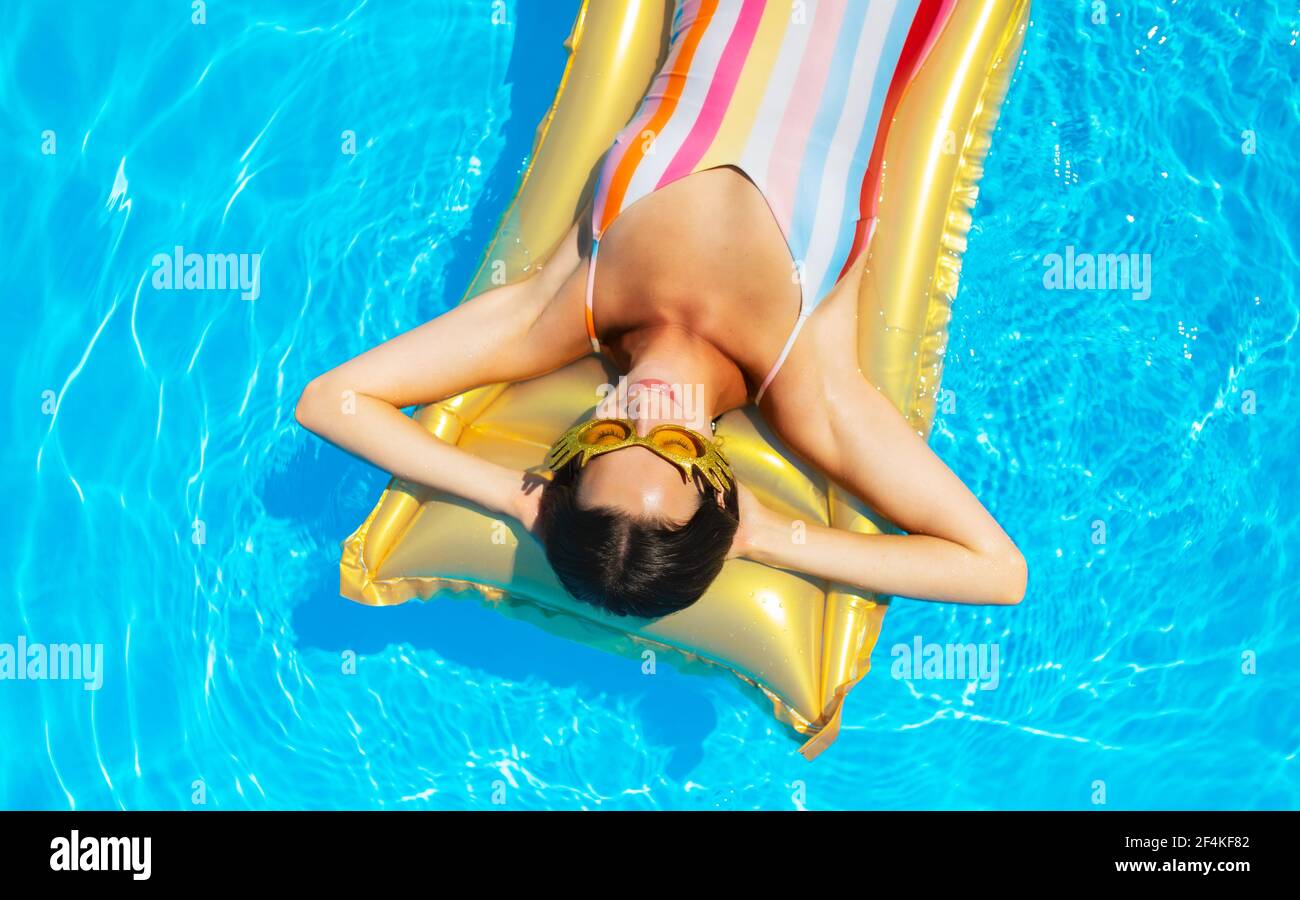 Top view of young woman in swimming pool outdoors on floating bed, relaxing. Stock Photo