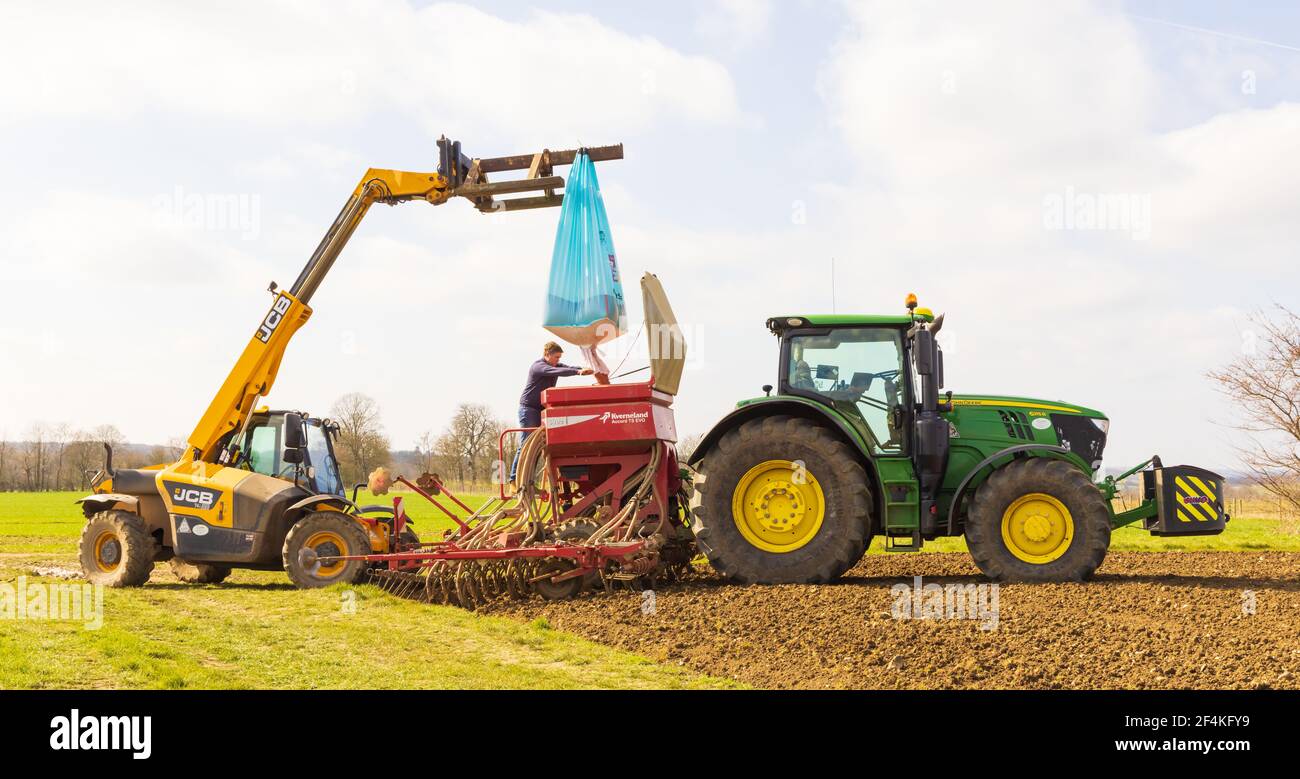 Farmer with a telehandler loading seeds into a seed driller attached to a tractor. Hertfordshire, UK. Stock Photo