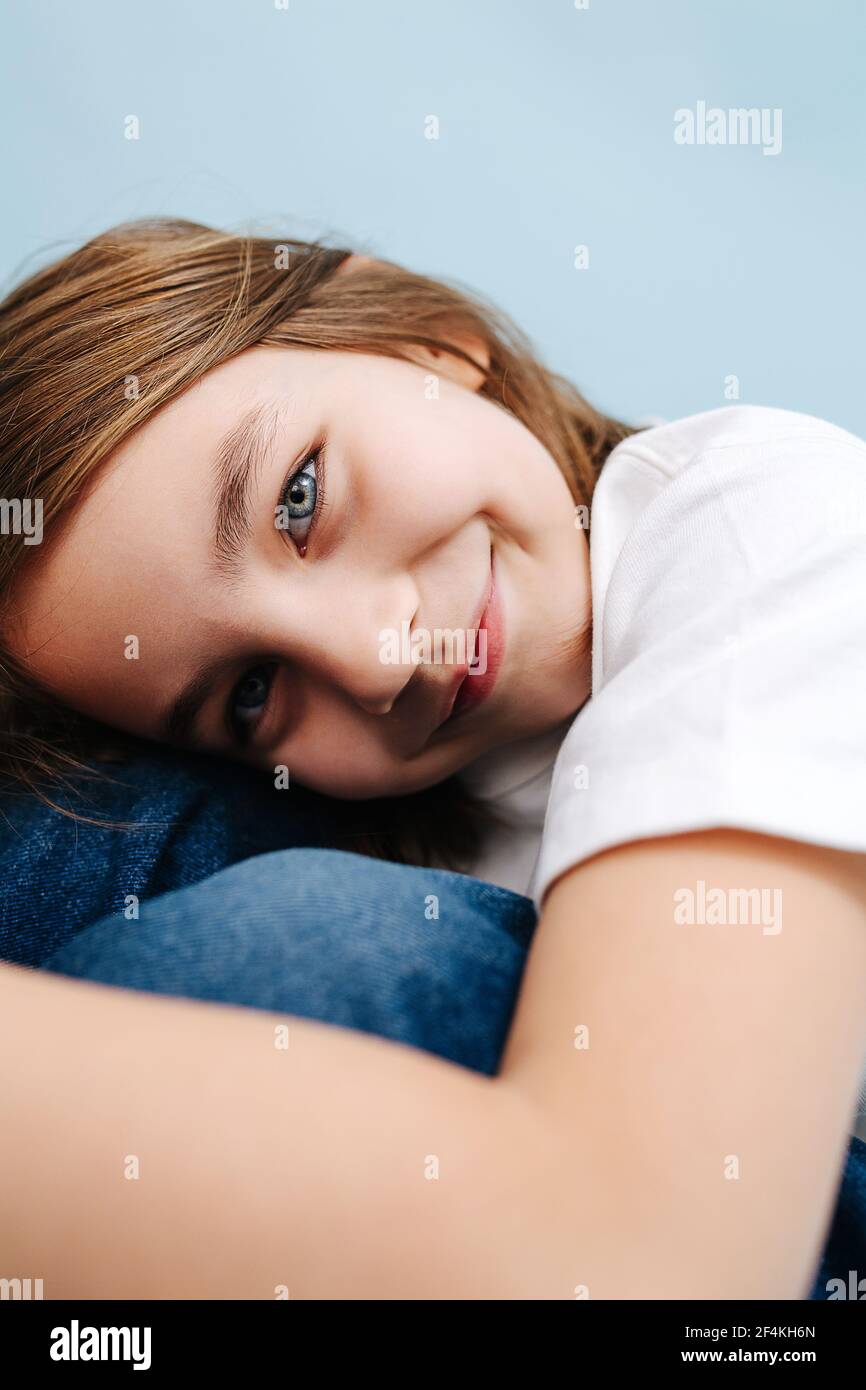 Pretty 9 year old girl resting head on her knees, on folded hands. She's sitting on the floor. Over blue background. She's wearing blue jeans and whit Stock Photo