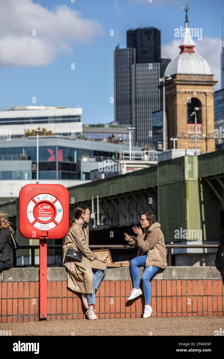 Londoner's sit out along the Thames River bankside at Southwark enjoying the early Spring sunshine during their lunchtime, England, United Kingdom Stock Photo