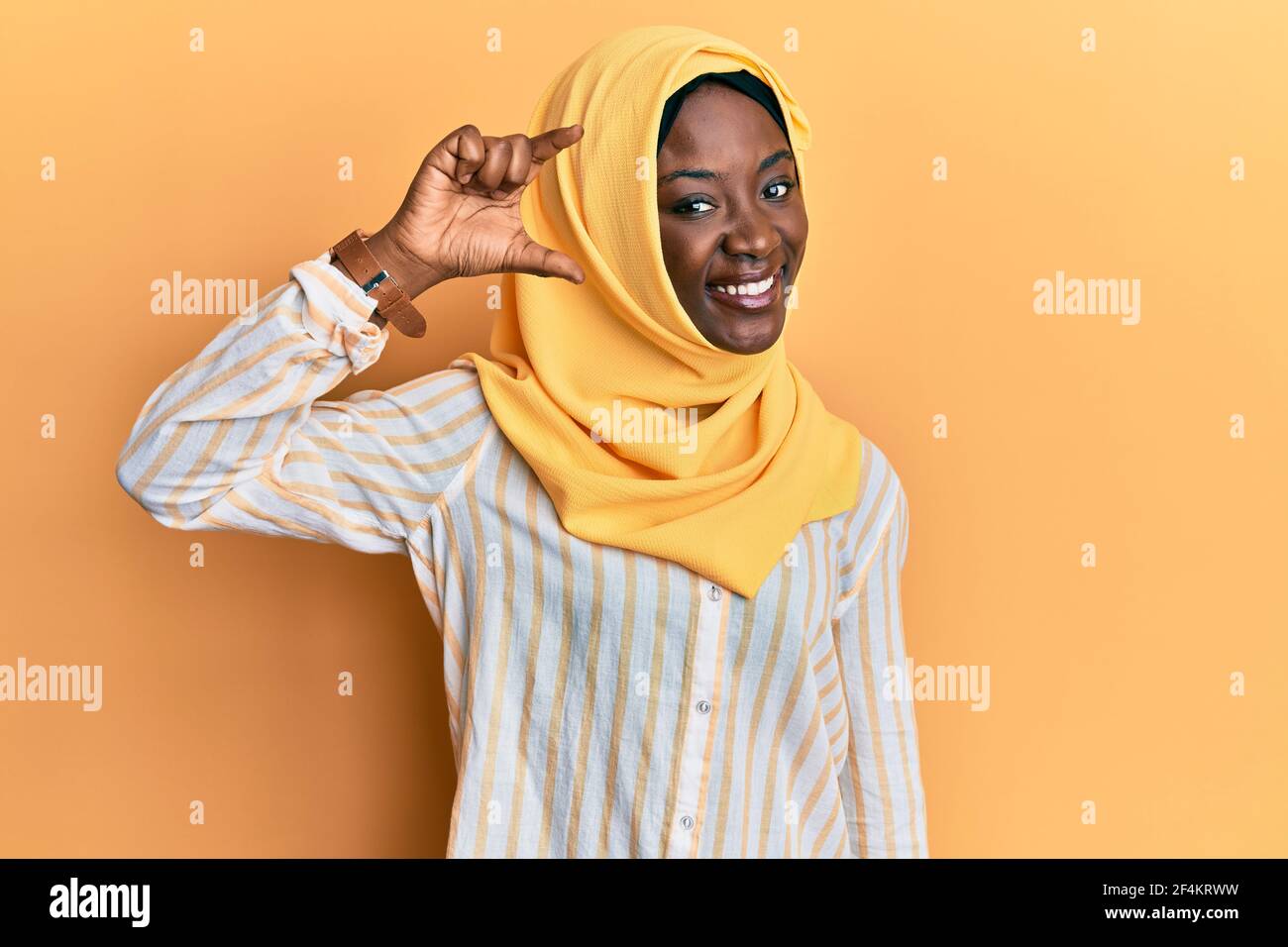 Beautiful african young woman wearing traditional islamic hijab scarf  smiling and confident gesturing with hand doing small size sign with fingers  loo Stock Photo - Alamy