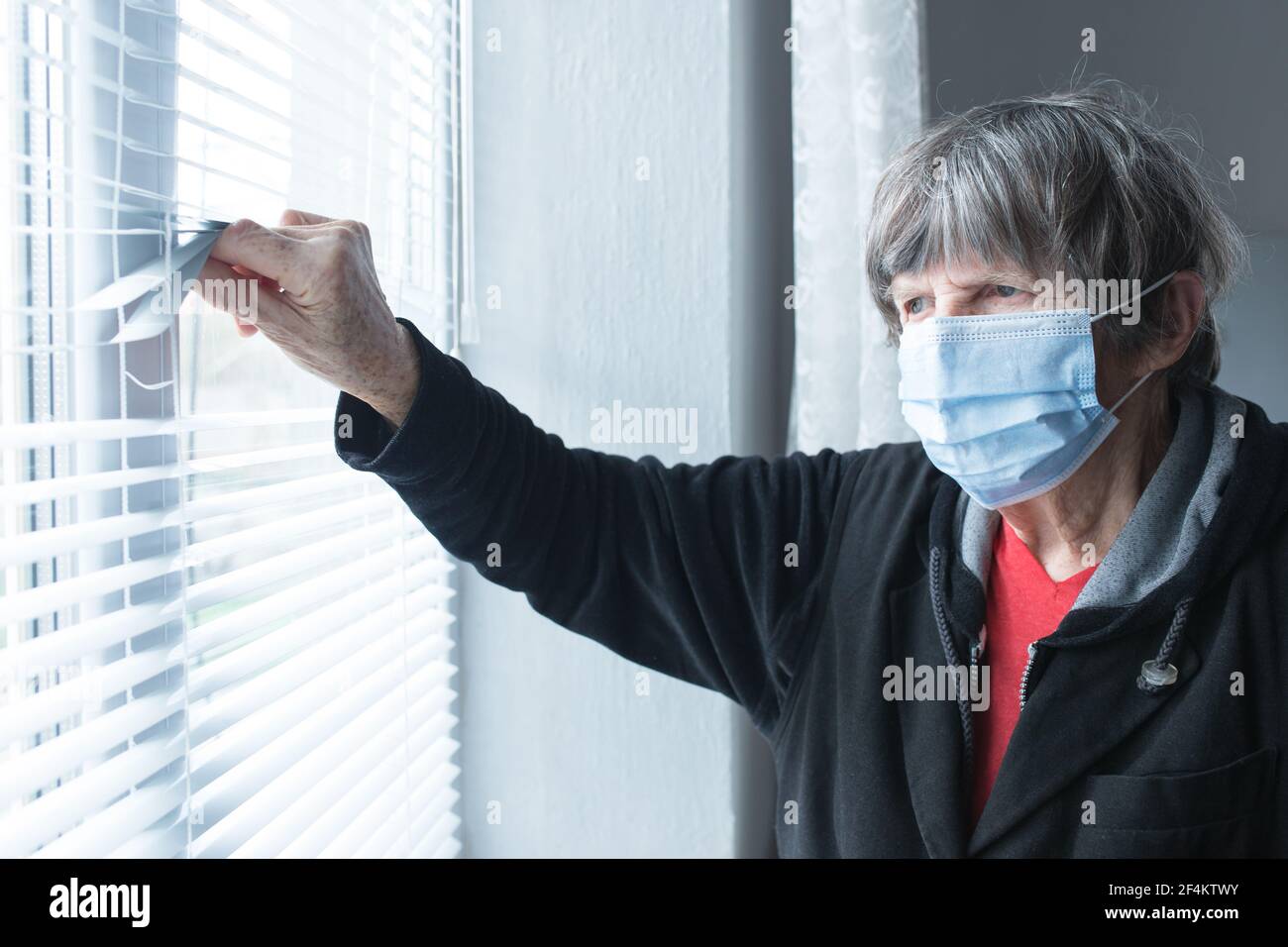 Old lady with medical mask at home during quarantine lokk out the window. Stock Photo