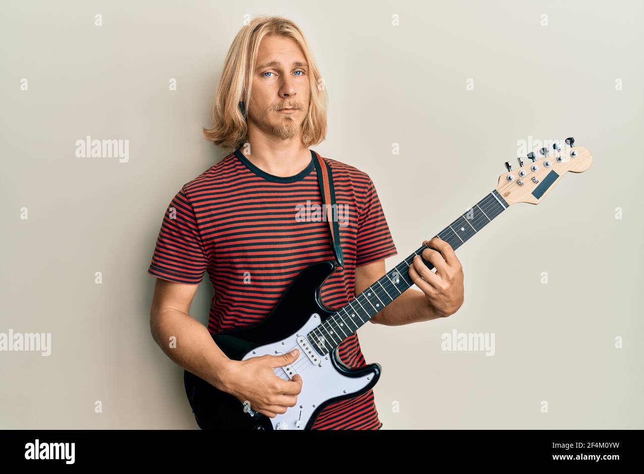 Caucasian young man with long hair playing electric guitar depressed