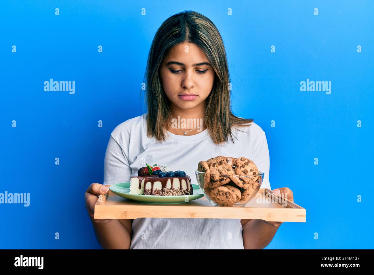 Sweets Sad Young latin woman holding cake sweets and cookies depressed and worry ...