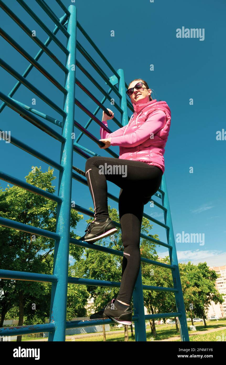 Young woman in sports clothes climbed on a sports complex during a workout view from below Stock Photo