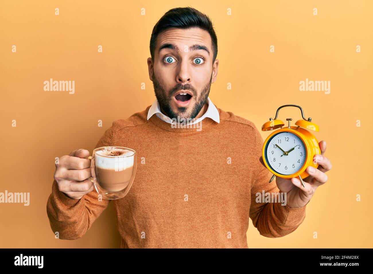 Young hispanic man holding coffee and alarm clock afraid and shocked with surprise and amazed