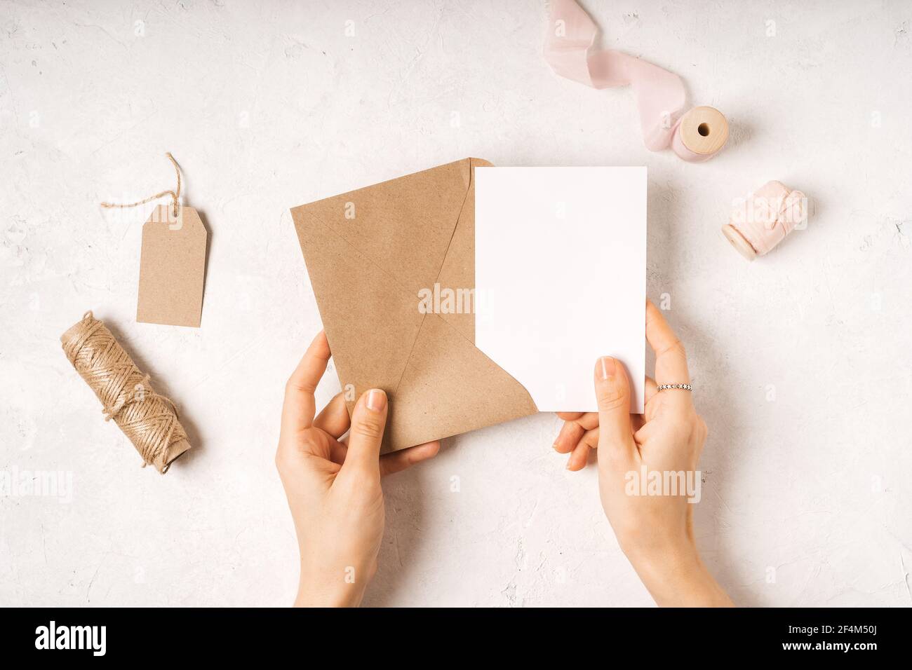 Blank white card with craft paper envelope in hands Stock Photo