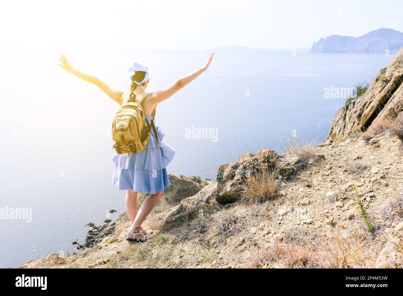 Traveler with a backpack on the top of the mountain against the background of the sea. Girl tourist enjoys the sea and sunlight. Travel, tourism and a Stock Photo