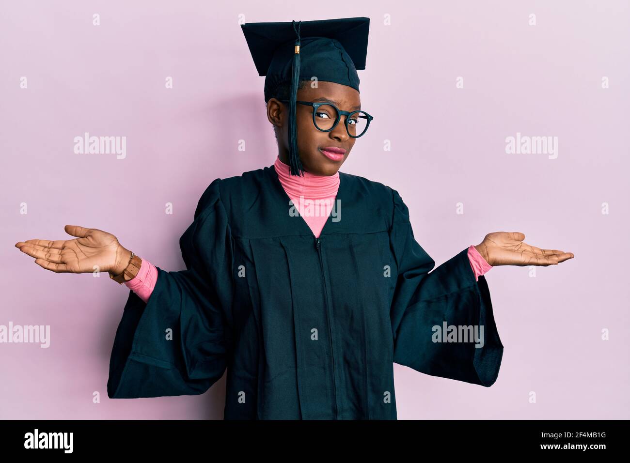 Young african american girl wearing graduation cap and ceremony robe clueless and confused expression with arms and hands raised. doubt concept. Stock Photo