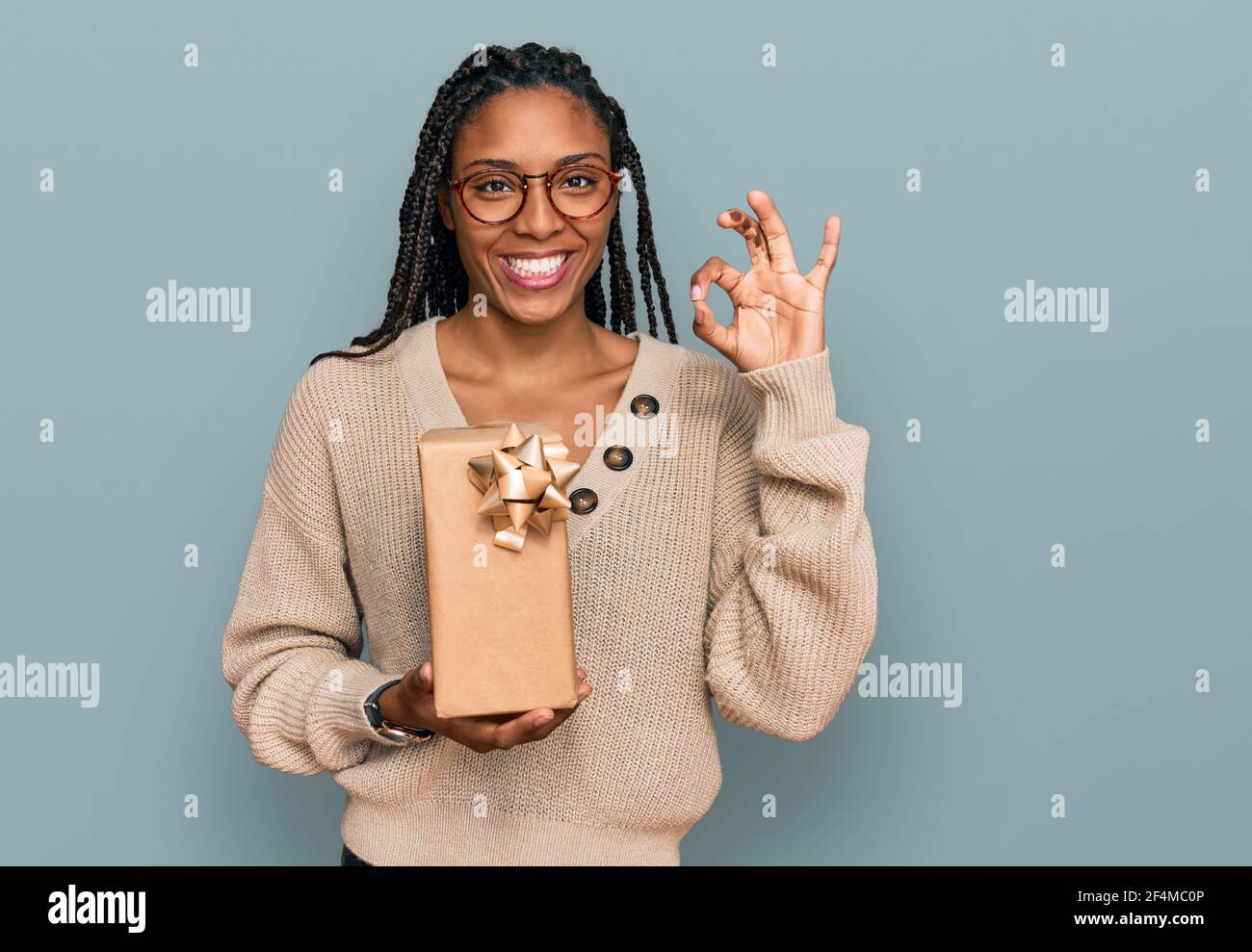 African american woman holding gift doing ok sign with fingers, smiling ...