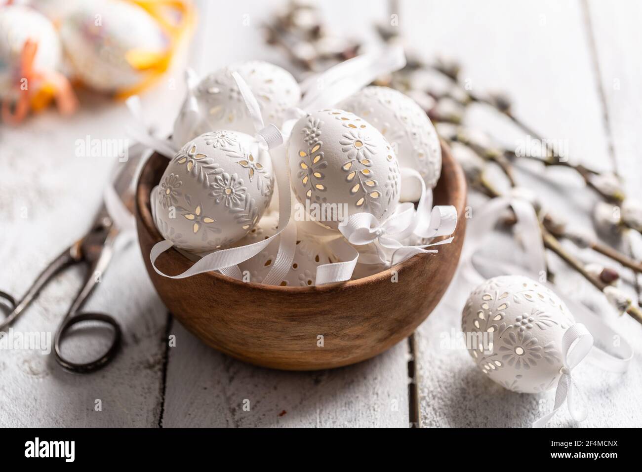 Handmade white easter eggs with willow catkins in a wooden bowl on wooden table. Stock Photo