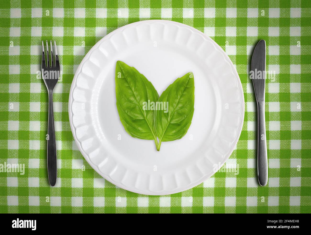 Vegan or vegetarian concept with green leafs on white plate against green checkered table cloth with fork and knife Stock Photo
