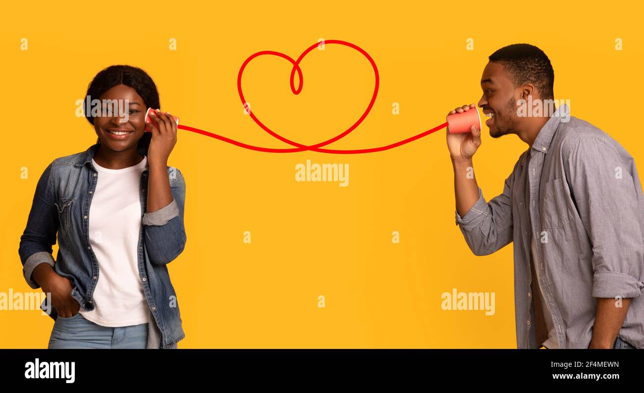 Affectionate black guy whisperinf words of love to girlfriend via tin phone Stock Photo