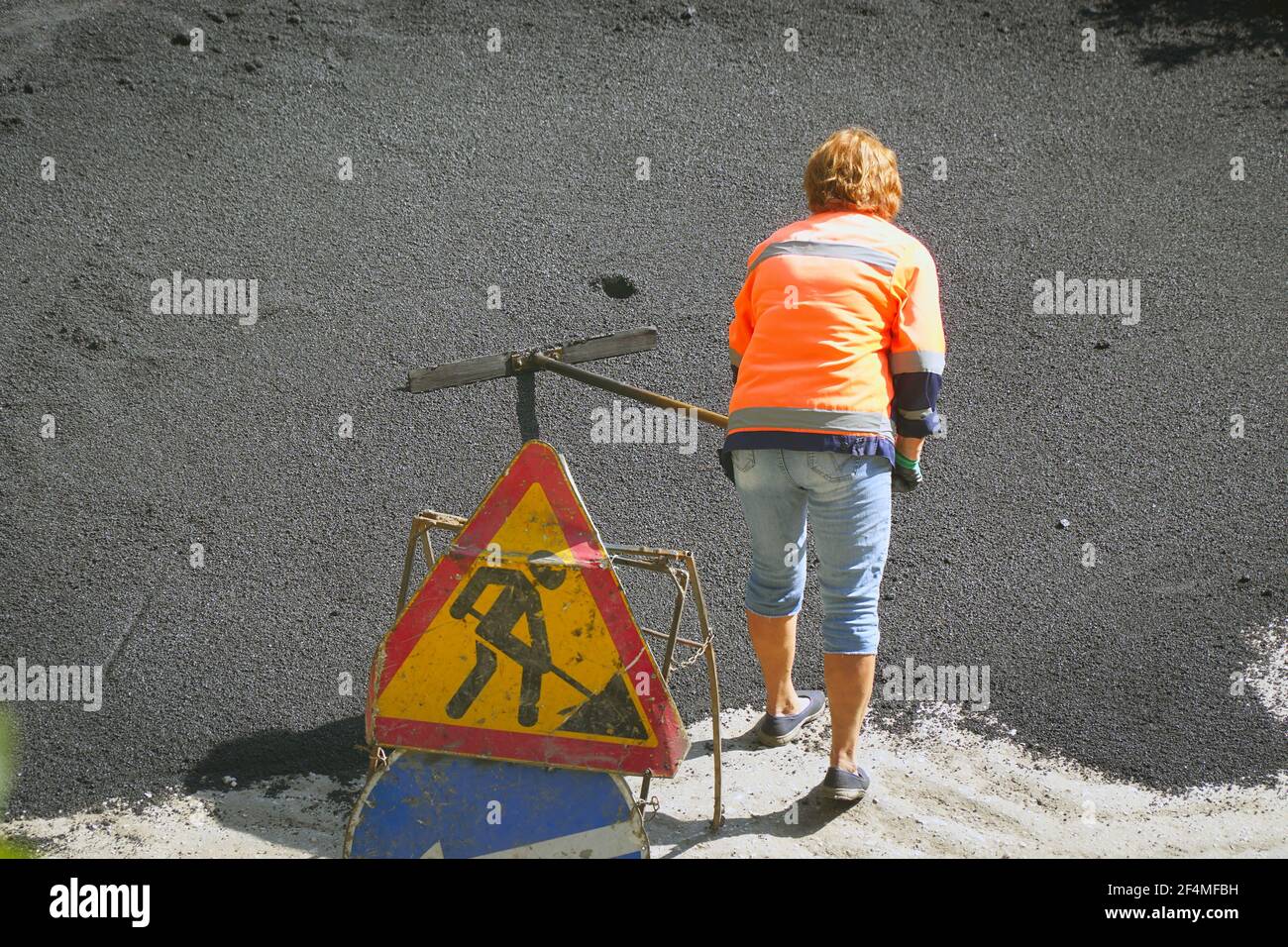 Road street repairing works. Female worker during asphalting road. Heavy female manual labor in construction Stock Photo