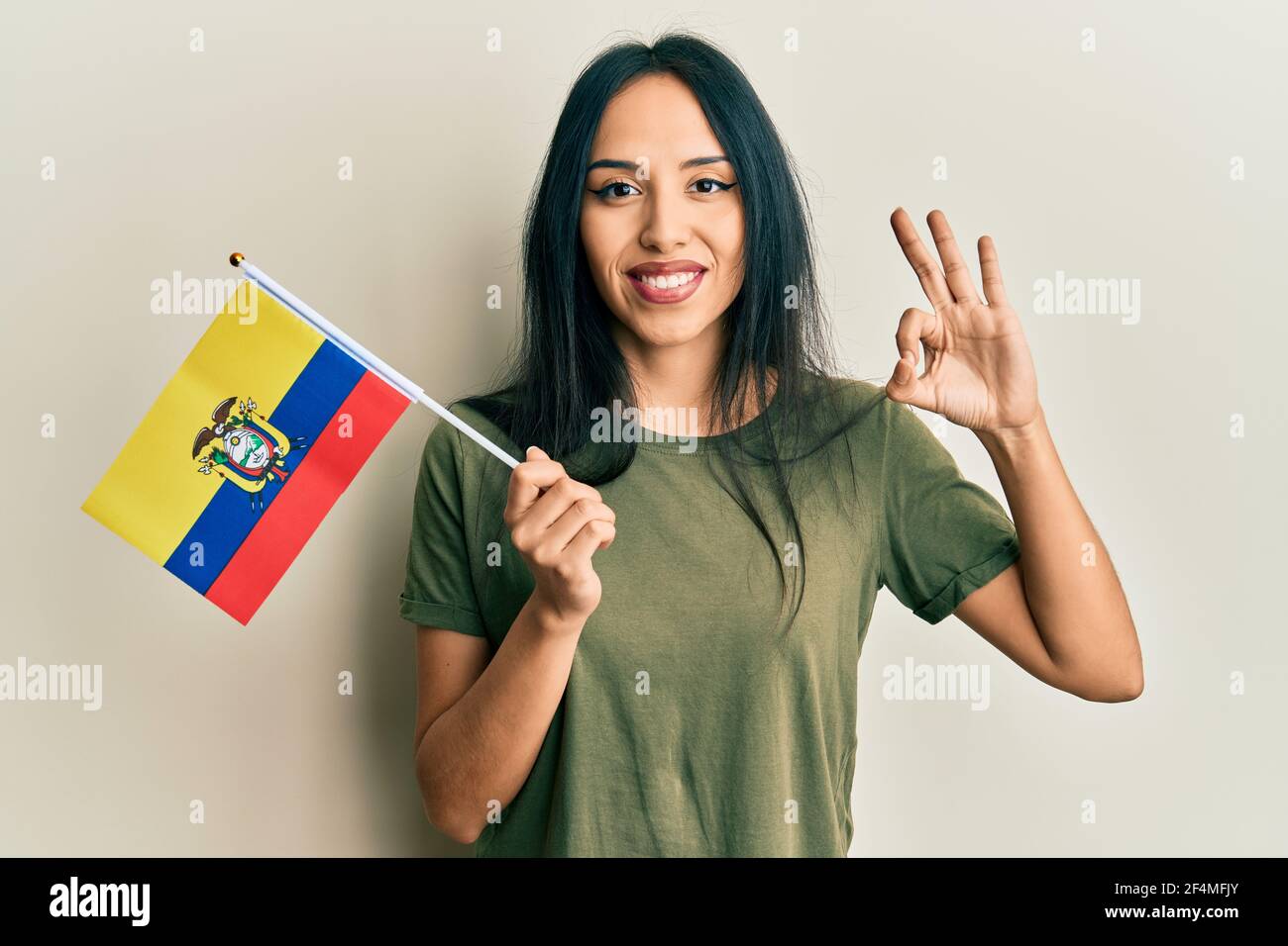 Young hispanic girl holding ecuador flag doing ok sign with fingers, smiling friendly gesturing excellent symbol Stock Photo