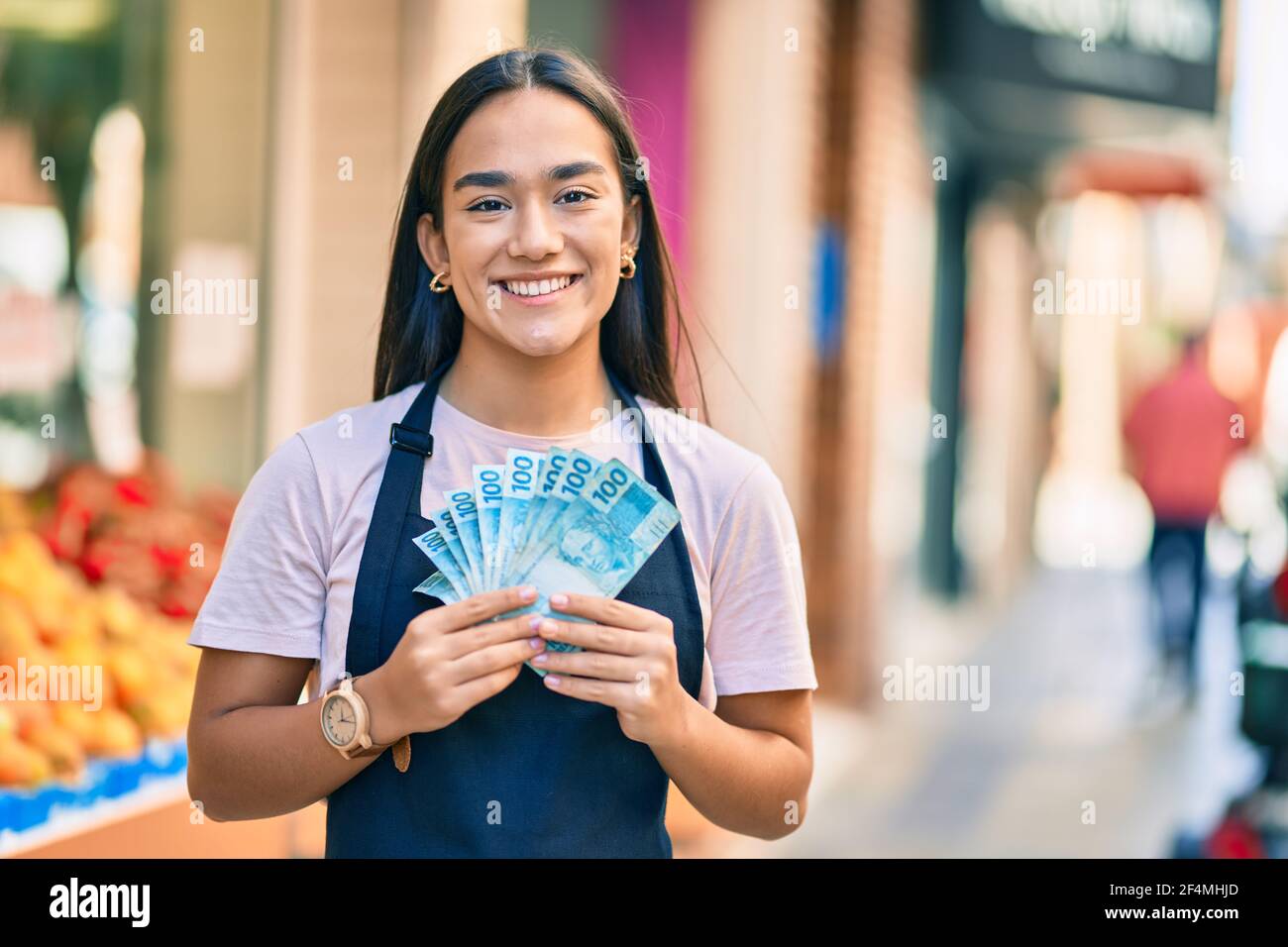 Shopkeeper Real Young latin shopkeeper girl smiling happy holding brazil real banknotes ...