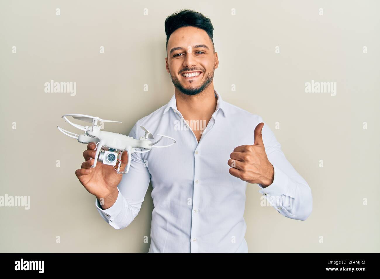 Young arab man using drone smiling happy and positive, thumb up doing ...