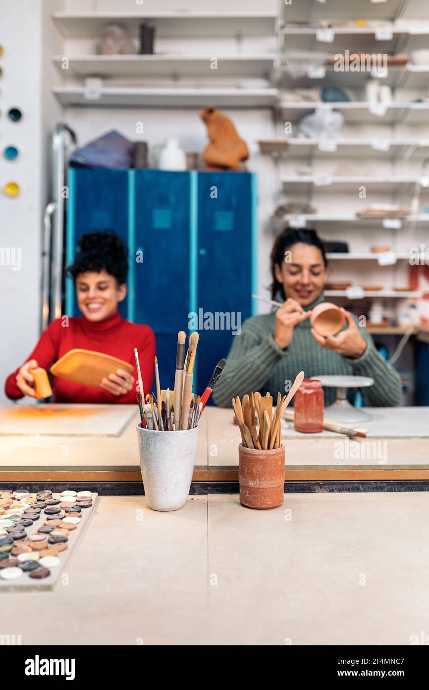 Stock photo of cheerful women in apron using paintbrush and talking