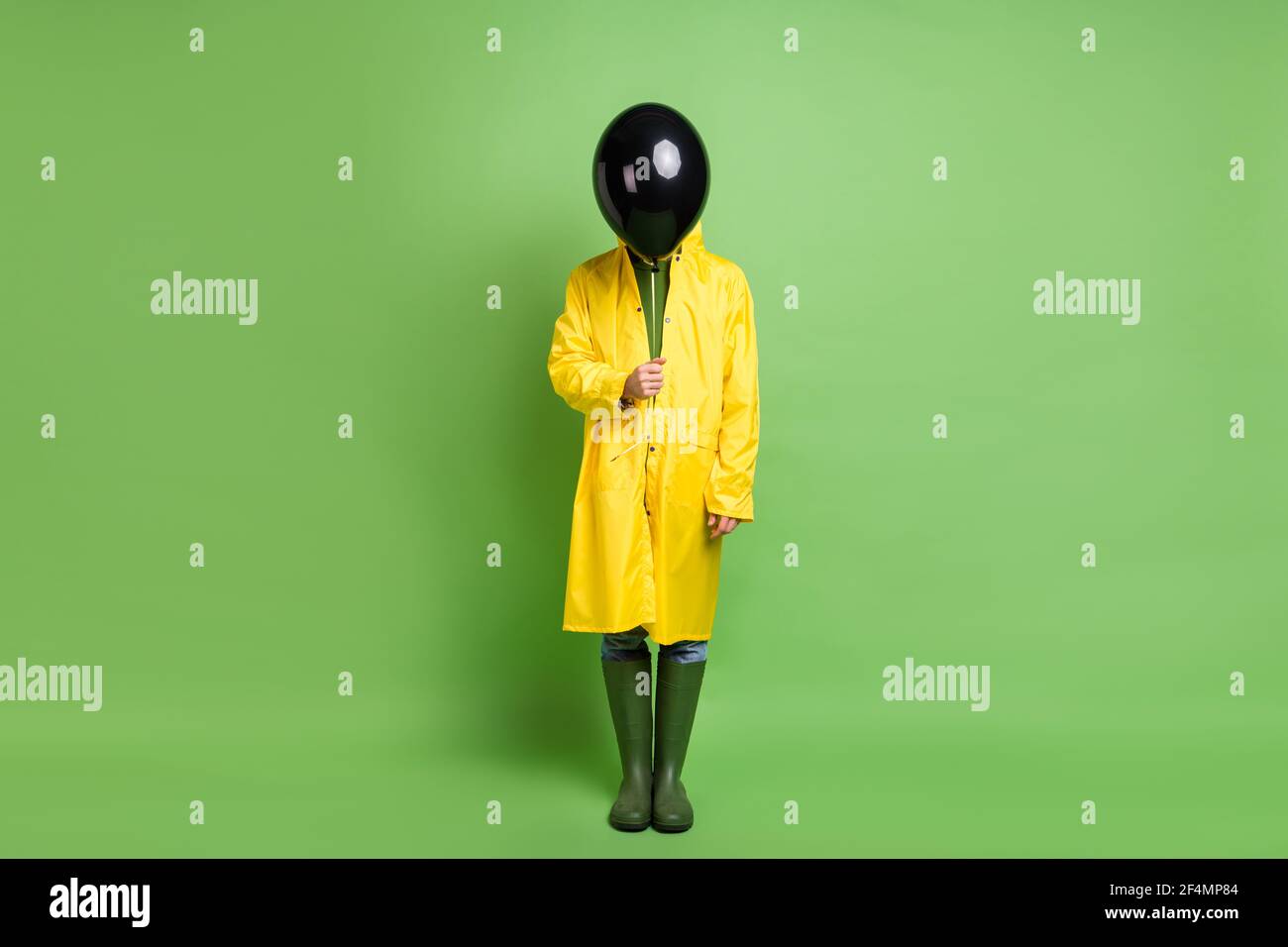 Full size photo of young man anonym close face air balloon party decoration wear raincoat isolated over green color background Stock Photo