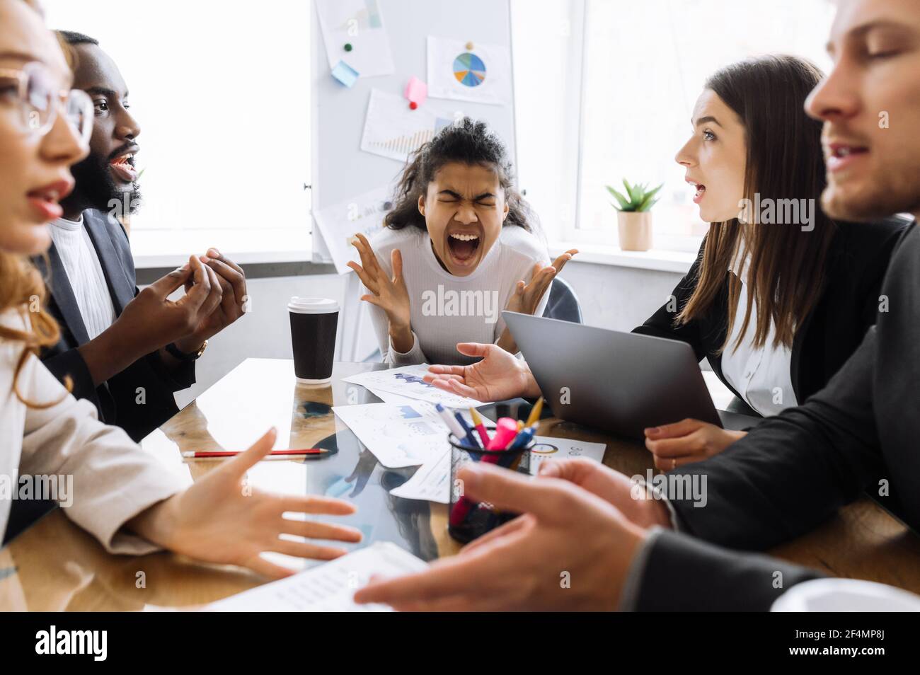 Exhausted male and female employees can't make agreement, arguing. Angry business people having a tense brainstorm, african american woman boss is screaming, feeling frustrated Stock Photo