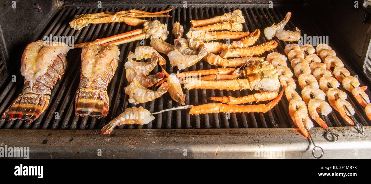 A collection of different kinds of seafood bbq cooking on a grill with lobster tail that is saddleback, tiger shrimp, shrimp on skewers, Alaskan snow Stock Photo