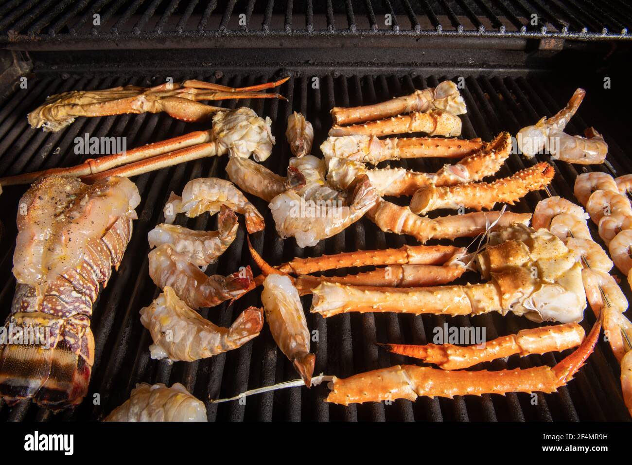 A collection of different kinds of seafood bbq cooking on a grill with lobster tail that is saddleback, tiger shrimp, shrimp on skewers, Alaskan snow Stock Photo