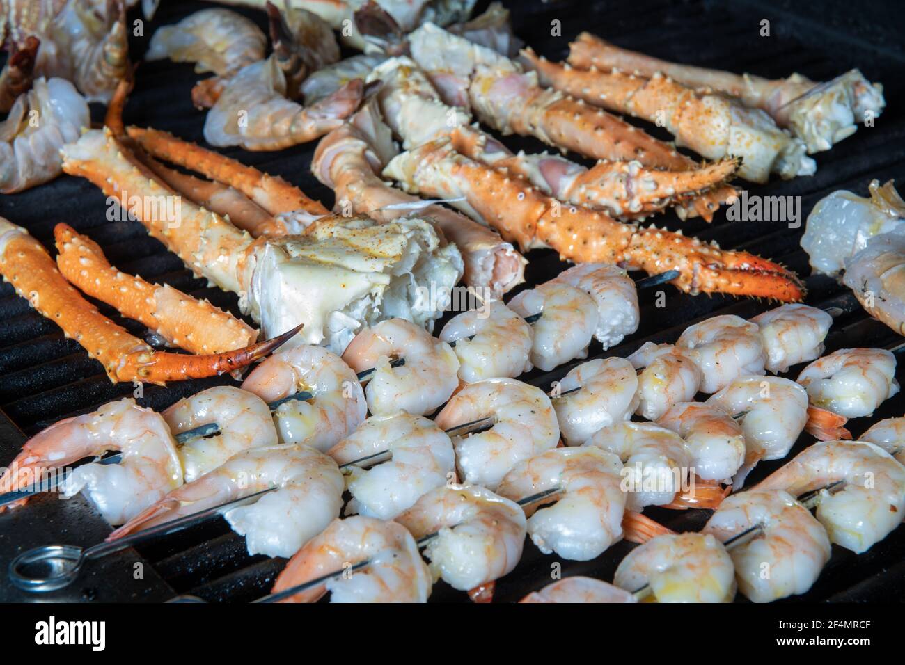 A collection of different kinds of seafood bbq cooking on a grill with shrimp on skewers, and Alaskan king crab Stock Photo