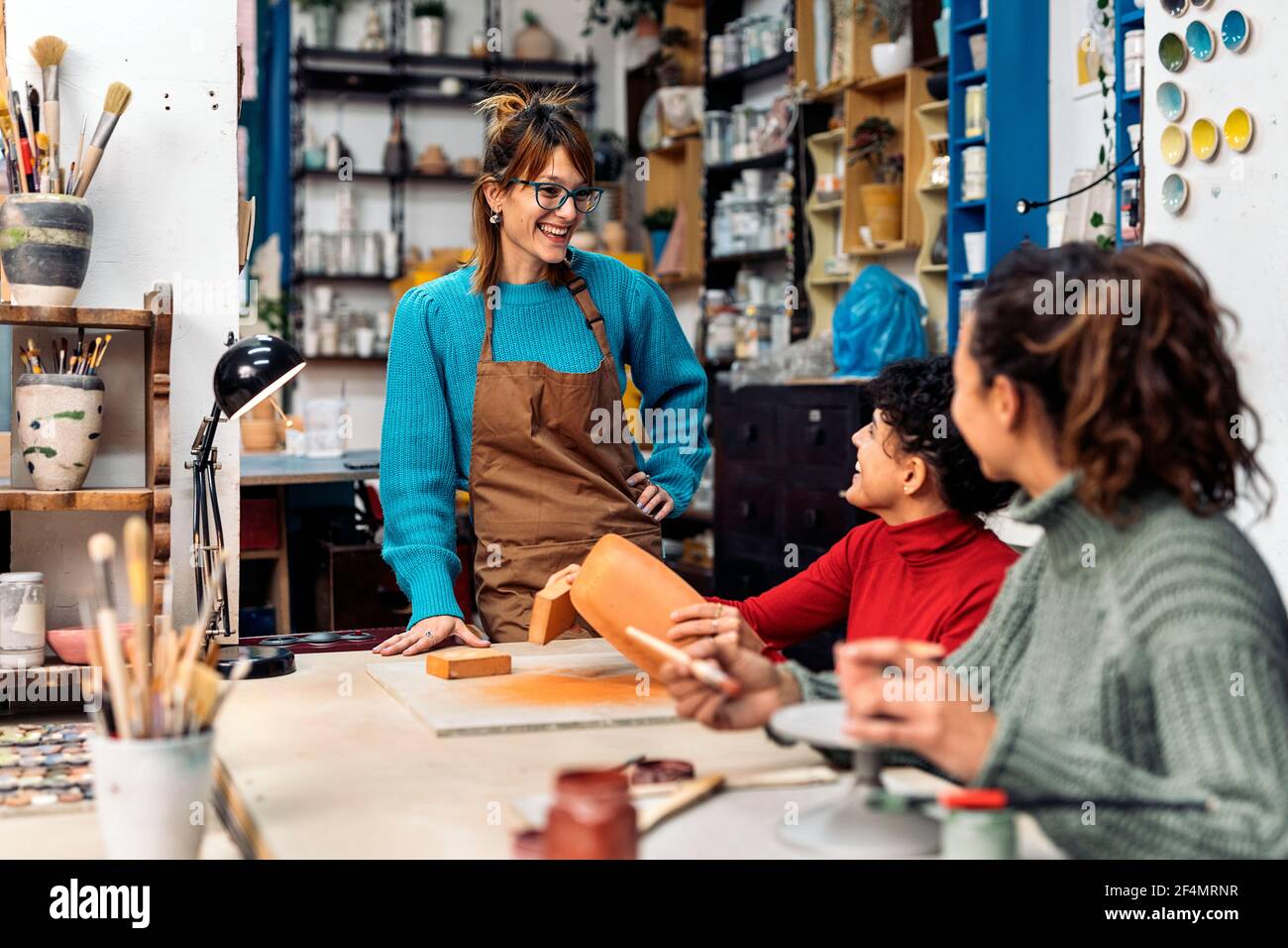 Stock photo of happy women in apron using clay and talking during