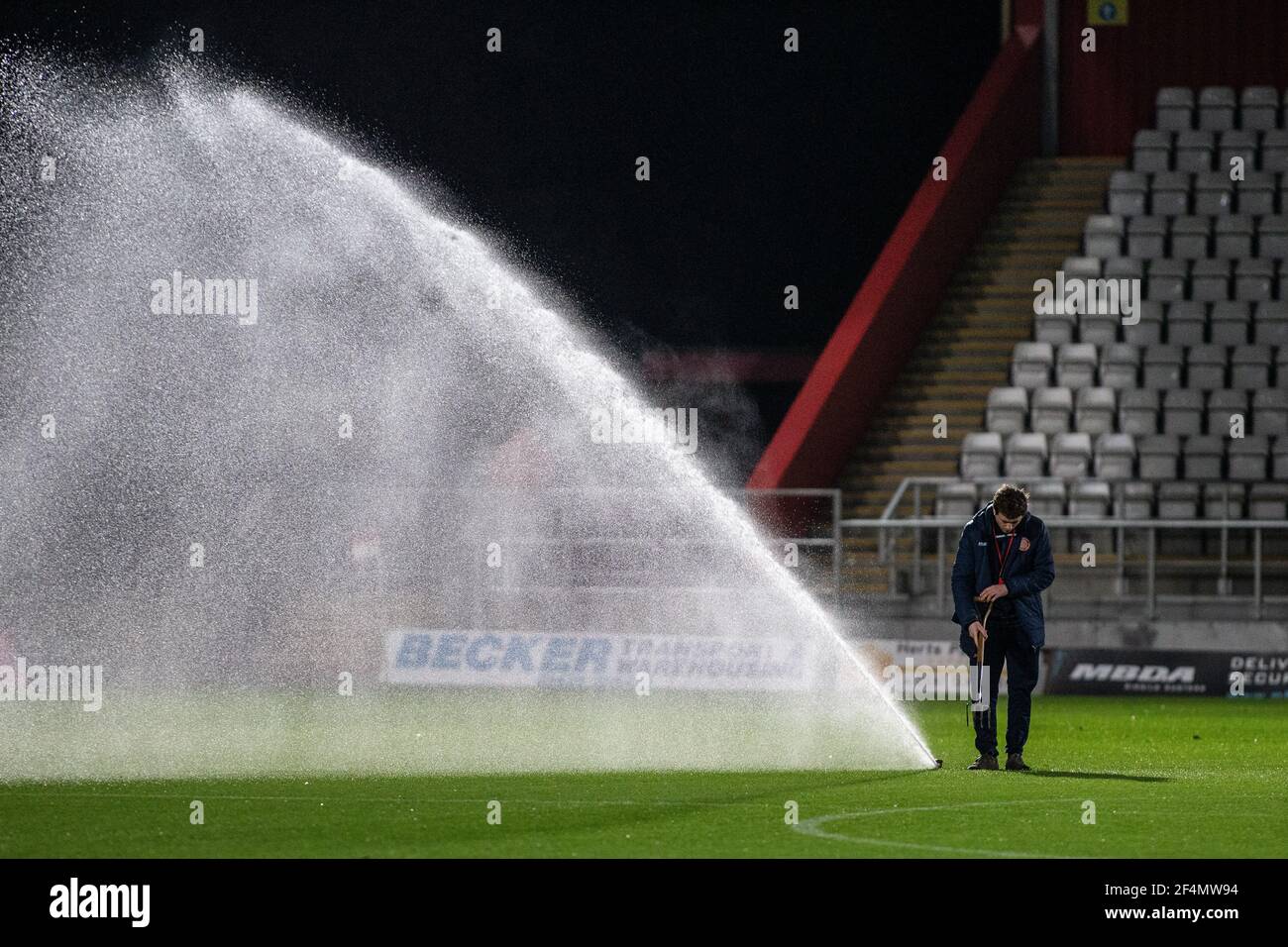 Groundsman ventilating football pitch standing beside sprinkler at lower league football stadium. Stock Photo